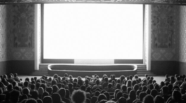 An audience sits before a large blank screen in a movie theater.