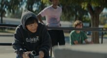 A teen boy holds up a small video camera at a skate park.