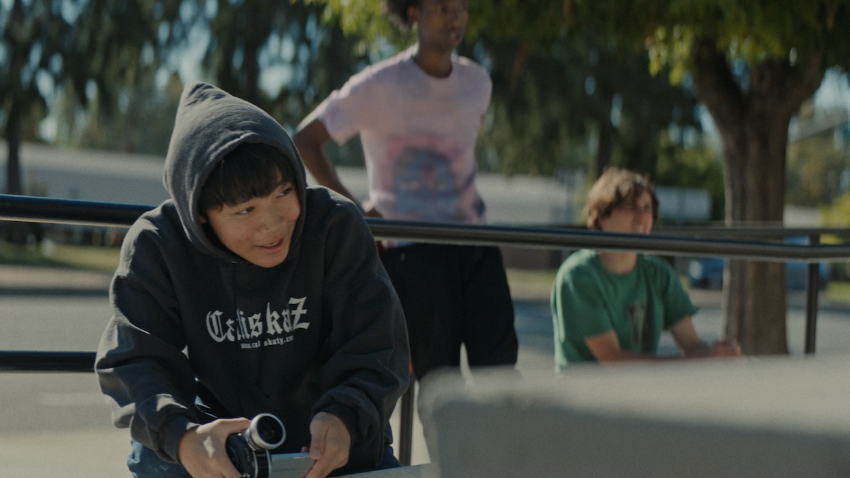 A teen boy holds up a small video camera at a skate park.