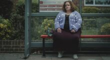 A woman sits on a bench waiting for a bus.