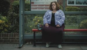 A woman sits on a bench waiting for a bus.