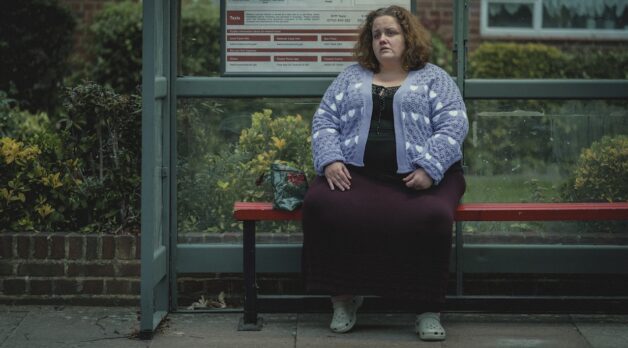 A woman sits on a bench waiting for a bus.