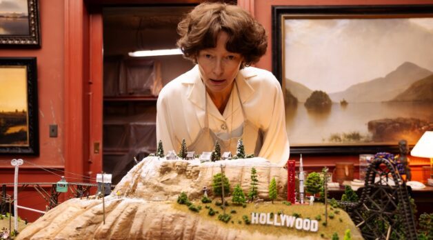 A woman leans over a miniature sculpted landscape that includes the Hollywood sign.