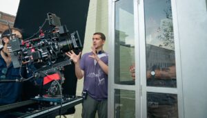 A man with headphones around his neck explains a shot to a camera on a film set.