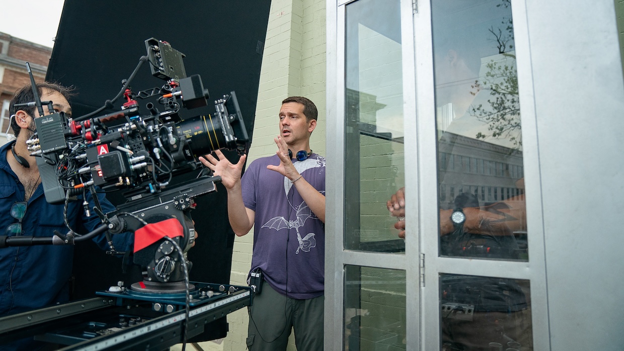 A man with headphones around his neck explains a shot to a camera on a film set.