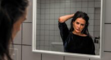 A middle-aged woman holds her hair in front of a mirror.