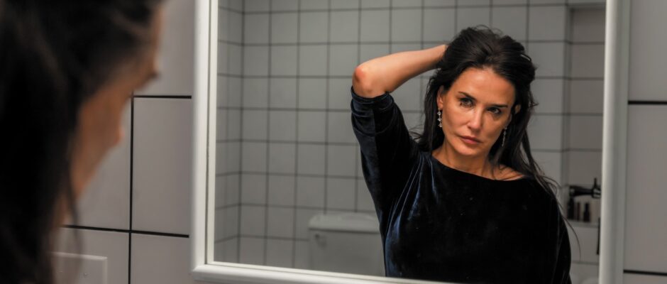 A middle-aged woman holds her hair in front of a mirror.