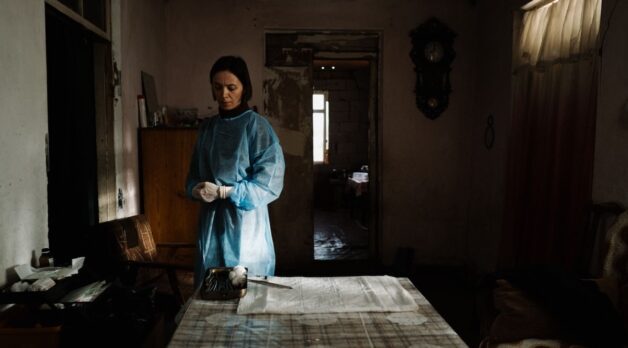 A woman in blue clothing stands in front of a table covered with newspapers.