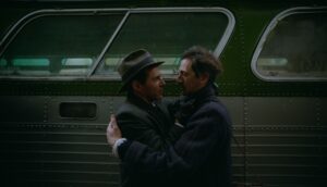 Two men hug in front of a bus.