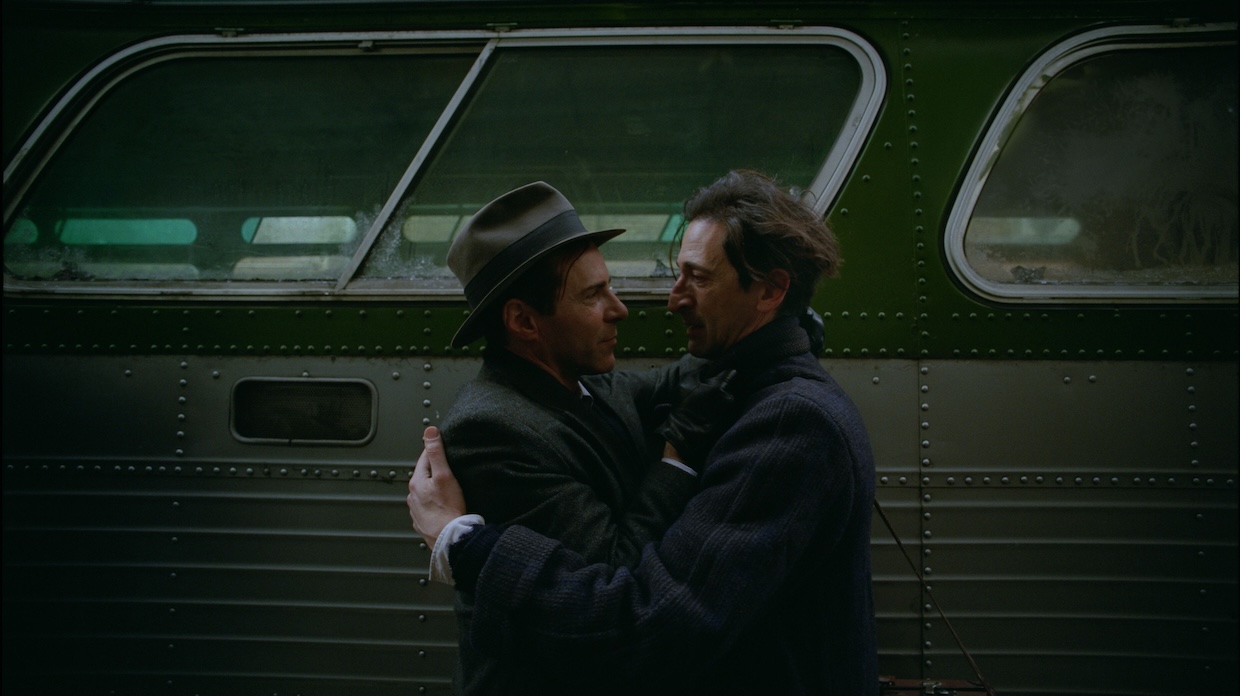 Two men hug in front of a bus.