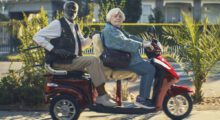 An elderly man and woman ride a motorized scooter.