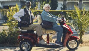 An elderly man and woman ride a motorized scooter.