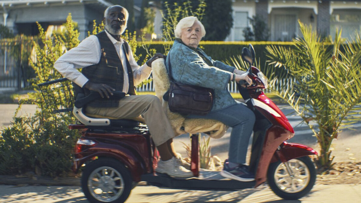 An elderly man and woman ride a motorized scooter.