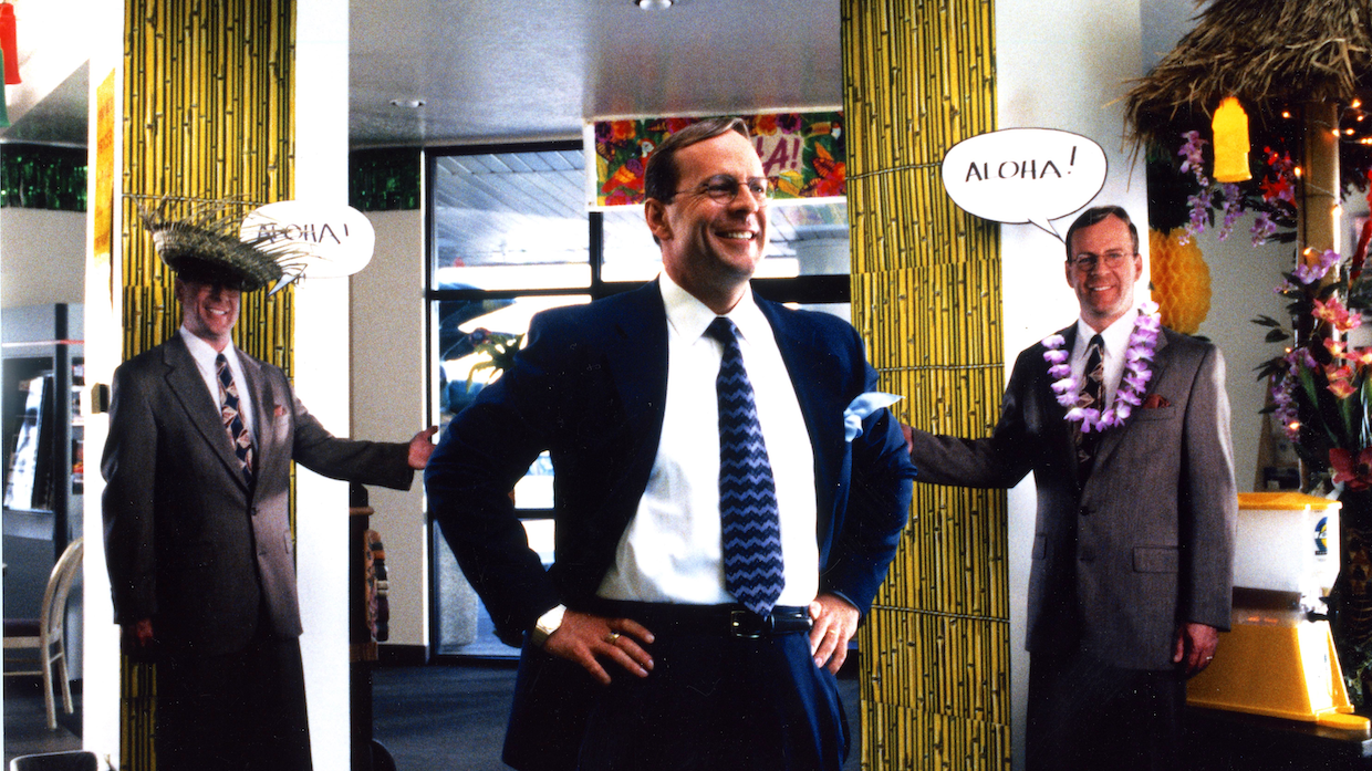 A man in a suit is flanked by two cardboard cutouts of himself.