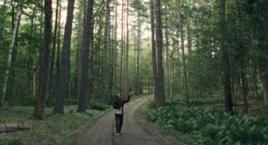 A man with a recording microphone capturing sounds in the woods.