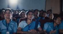 An audience of female Indian nurses sits in a movie theater watching a film.