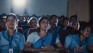 An audience of female Indian nurses sits in a movie theater watching a film.