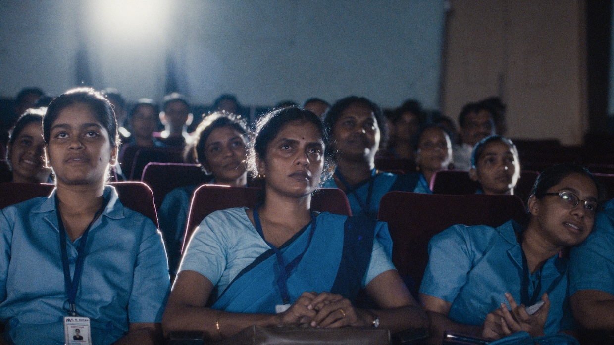 An audience of female Indian nurses sits in a movie theater watching a film.