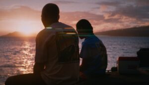 Two people sit on a beach at sunset.