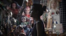 A young gymnast stands at night before a display of dolls.