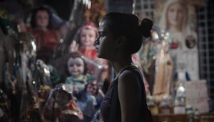 A young gymnast stands at night before a display of dolls.