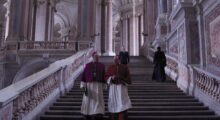 Two Catholic cardinals walk down a stairway in an elaborate building.