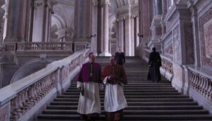 Two Catholic cardinals walk down a stairway in an elaborate building.