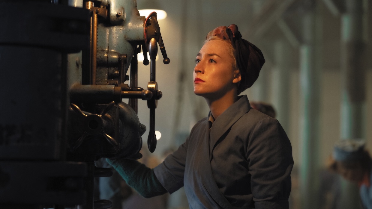 A woman stares into the distance while on the floor of an industrial factory.