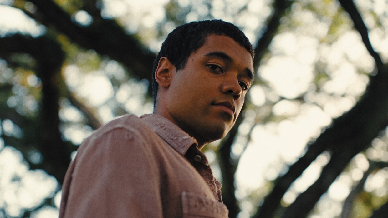 A young man stares directly at you while outside.