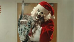 A clown in a Santa suit wields a chainsaw.