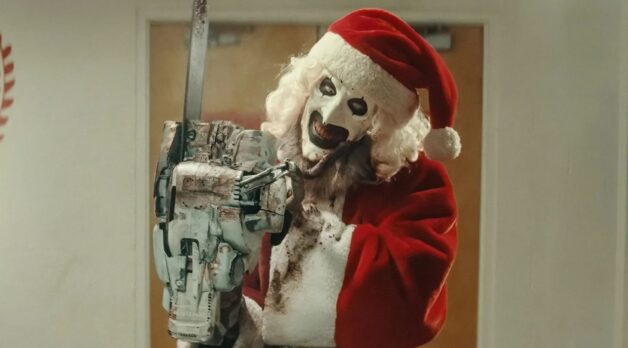 A clown in a Santa suit wields a chainsaw.