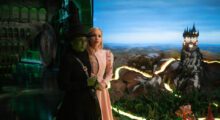 A green witch and white woman stand together against a very fake-looking background.