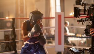 A woman in boxing gloves faces a camera on a film set.