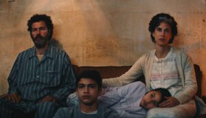 A Palestinian family sits in their living room, worried expressions on all of their faces.