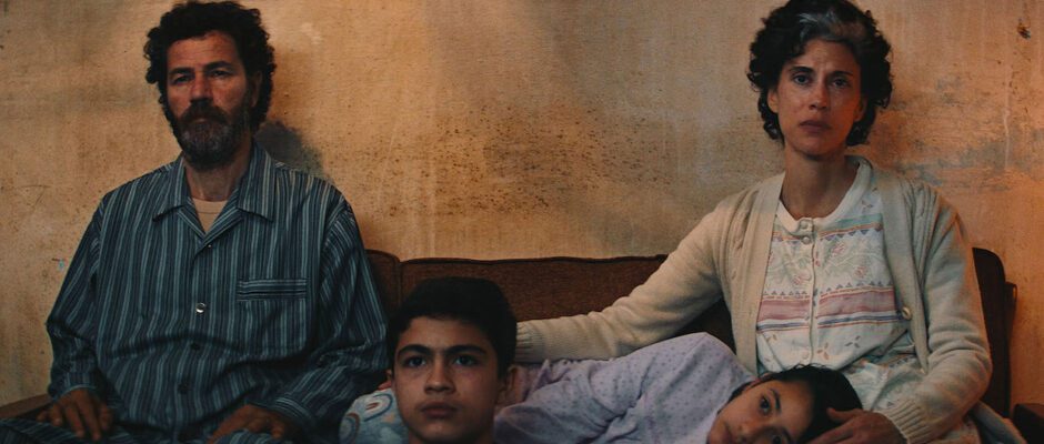 A Palestinian family sits in their living room, worried expressions on all of their faces.