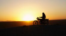 A silhouetted Iranian woman is riding a motorcycle against the sunset.