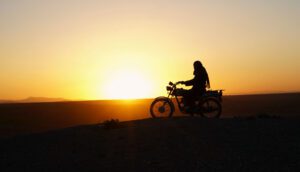 A silhouetted Iranian woman is riding a motorcycle against the sunset.