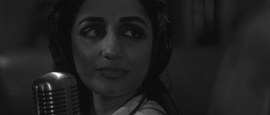 Black-and-white close-up of a women wearing headphones in front of a microphone.