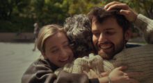 Two adult siblings facing the camera hug their father, who is facing away.