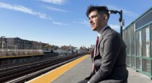 A young man in a suit is waiting at a train station.