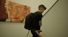 A man wearing a backpack is walking past a painting of Ruth Bader Ginsburg.