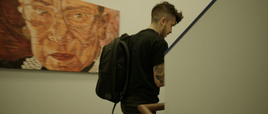 A man wearing a backpack is walking past a painting of Ruth Bader Ginsburg.