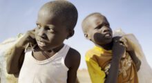 Two-shot of young Sudanese boys comparing bags over their shoulders.