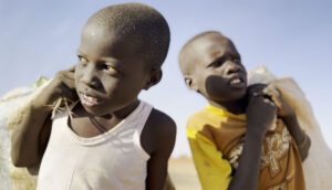 Two-shot of young Sudanese boys comparing bags over their shoulders.