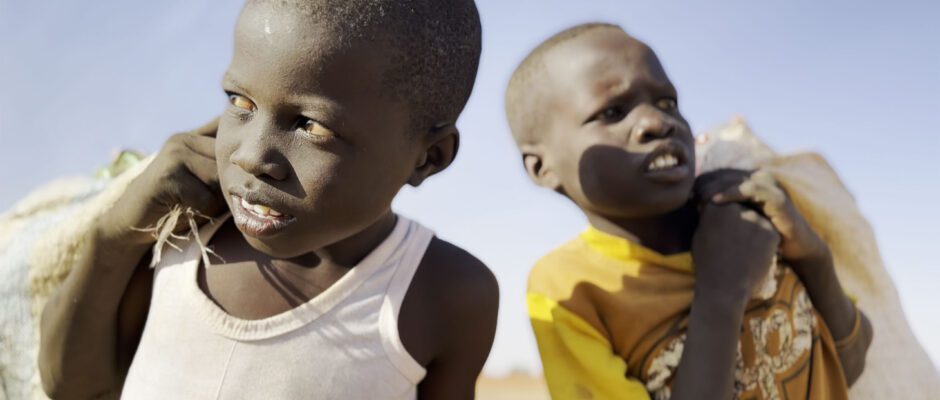 Two-shot of young Sudanese boys comparing bags over their shoulders.