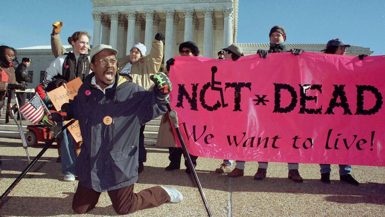 A disabilities rights protest with a banner reading "Not Dead, We Want To Live" visible.