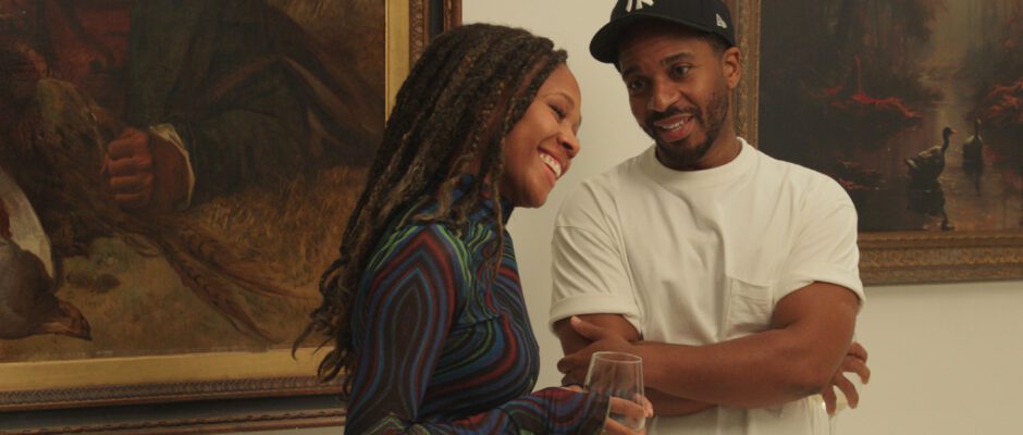 A Black man in a Yankees cap and a Black woman are standing together in an art gallery.