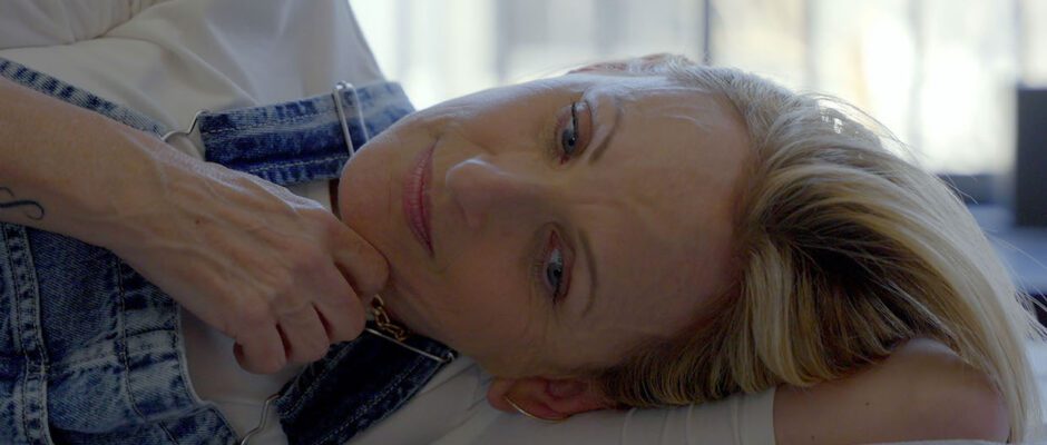 Blonde-haired actress Marlee Matlin lays down on a bed, lightly smiling and looking into the camera.