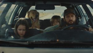 A white man, two white children, and a golden retriever are sitting in a car.