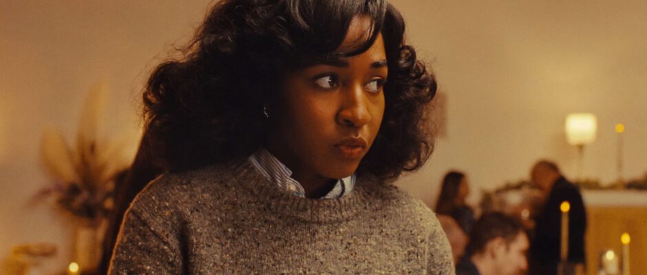 A young Black woman wears a gray sweater and looks off into the corner of a room.